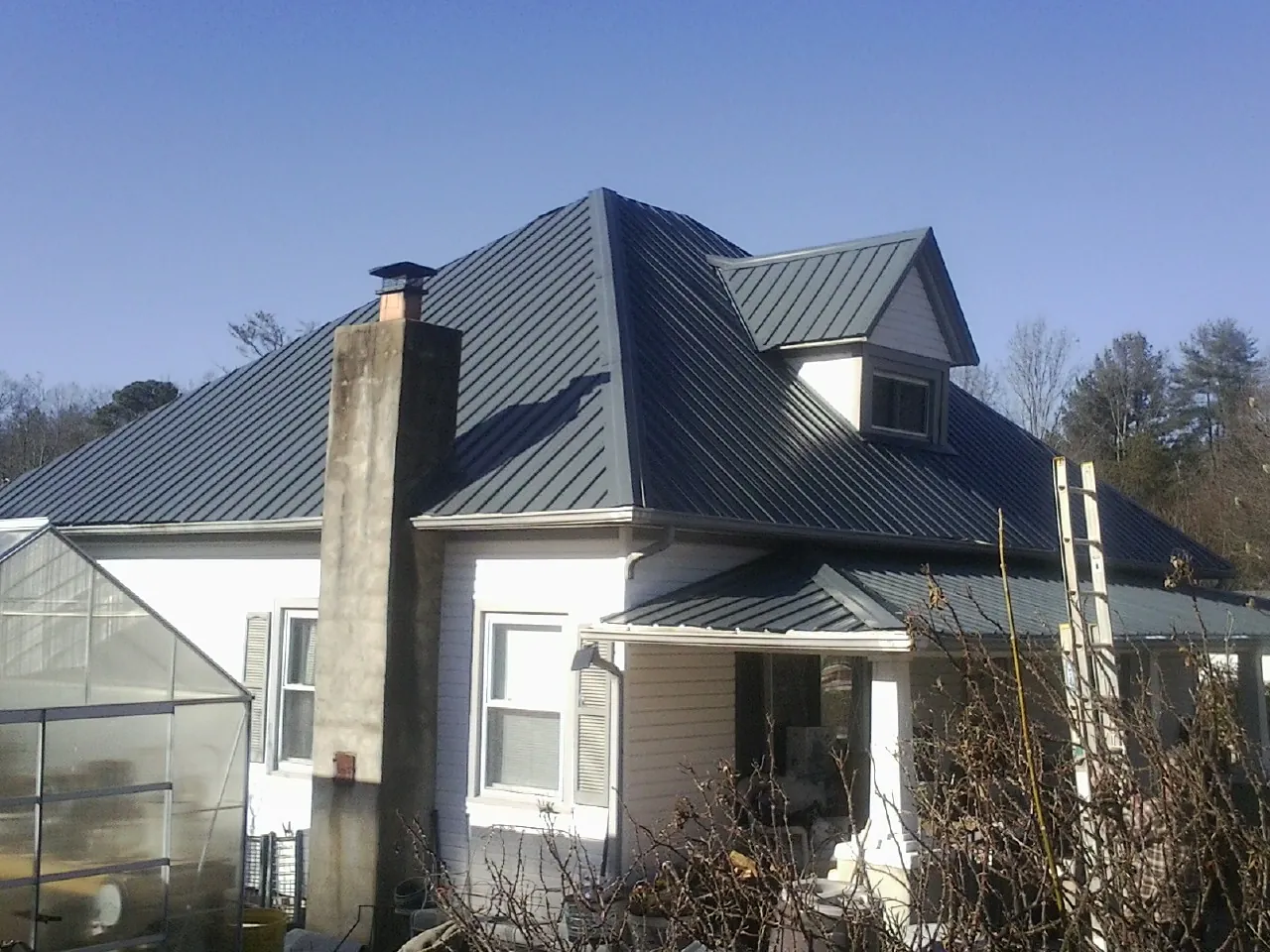 Dark blue standing seam metal roof on a white farmhouse with dormer — Slate & Tile Roof Repair by Roofing Brothers in Dawson