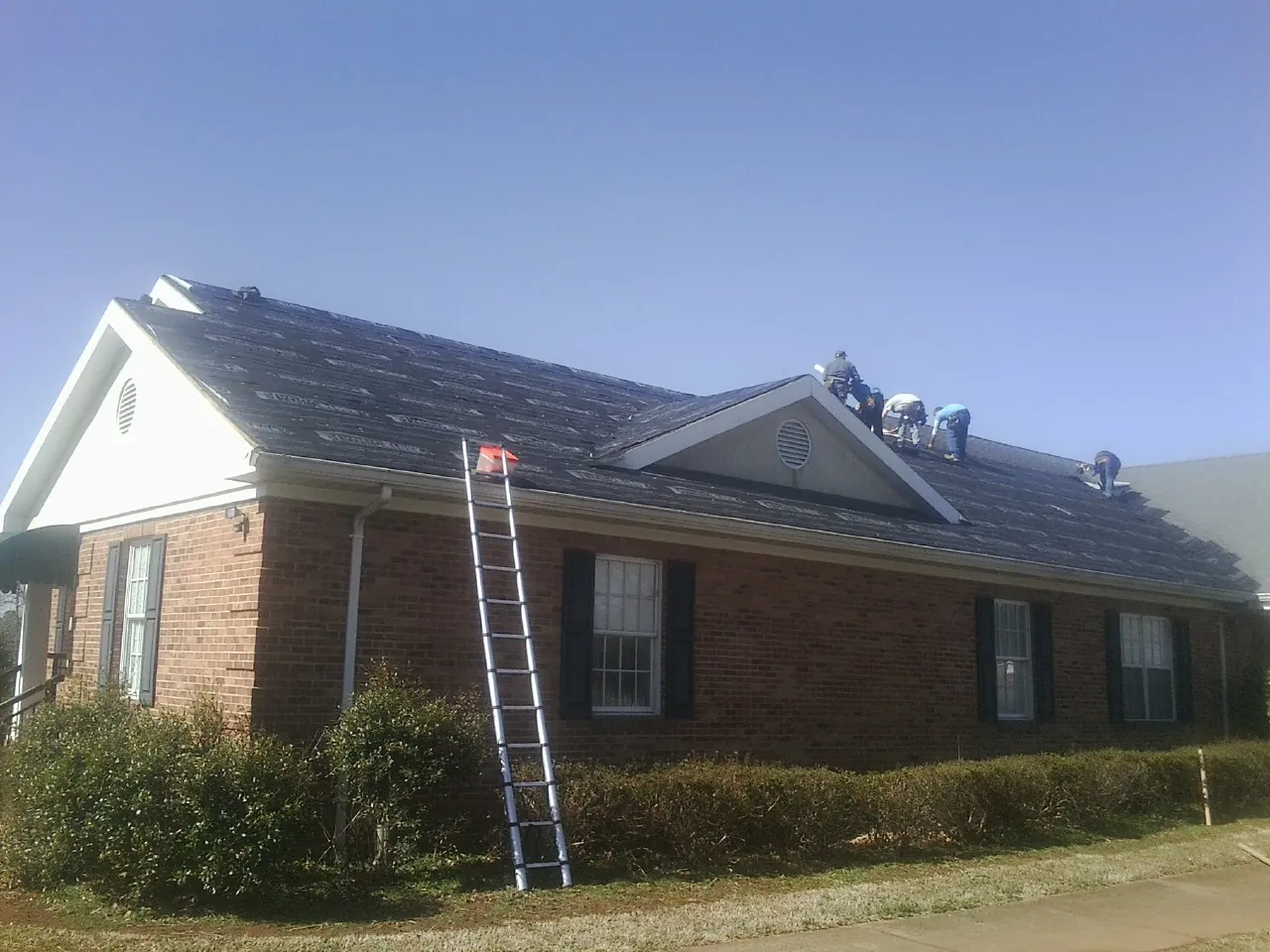 Crew tearing shingles off a brick ranch roof with a ladder set — Emergency Roof Repair work by our crew in Dawson